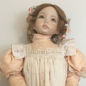 19-inch modern doll with brown hair in milkmaid braid with painted eyes and peach dress with white pinafore