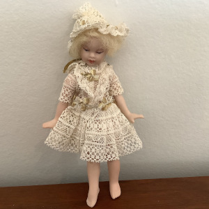 Small, blond, light-skinned doll wearing dress made entirely out of lace and matching bonnet