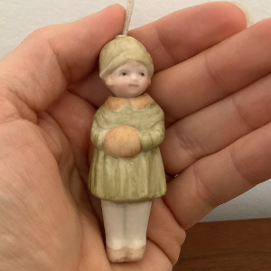 Small pastoral figurine appended on a string from the head, in green coat with short blond hair and light skin