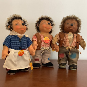 Group of toy hedgehogs, one with significant sun damage and two in fairly good shape, wearing farm clothing