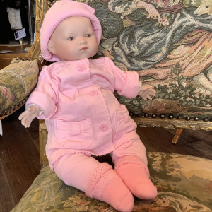 Reproduction Baby Bye-Lo doll in modern pink onesie with matching hat, seated on a chair