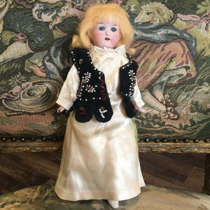 Vintage fashion doll with yellow hair and green sleep eyes wearing a yellow satin dress and a velvet dress with hand-beaded design and hanging ribbons