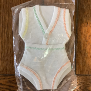 A set of top and bottom white underwear, edged in deliberately asymmetrical pattern of yellow, green and orange stitching, on a display card