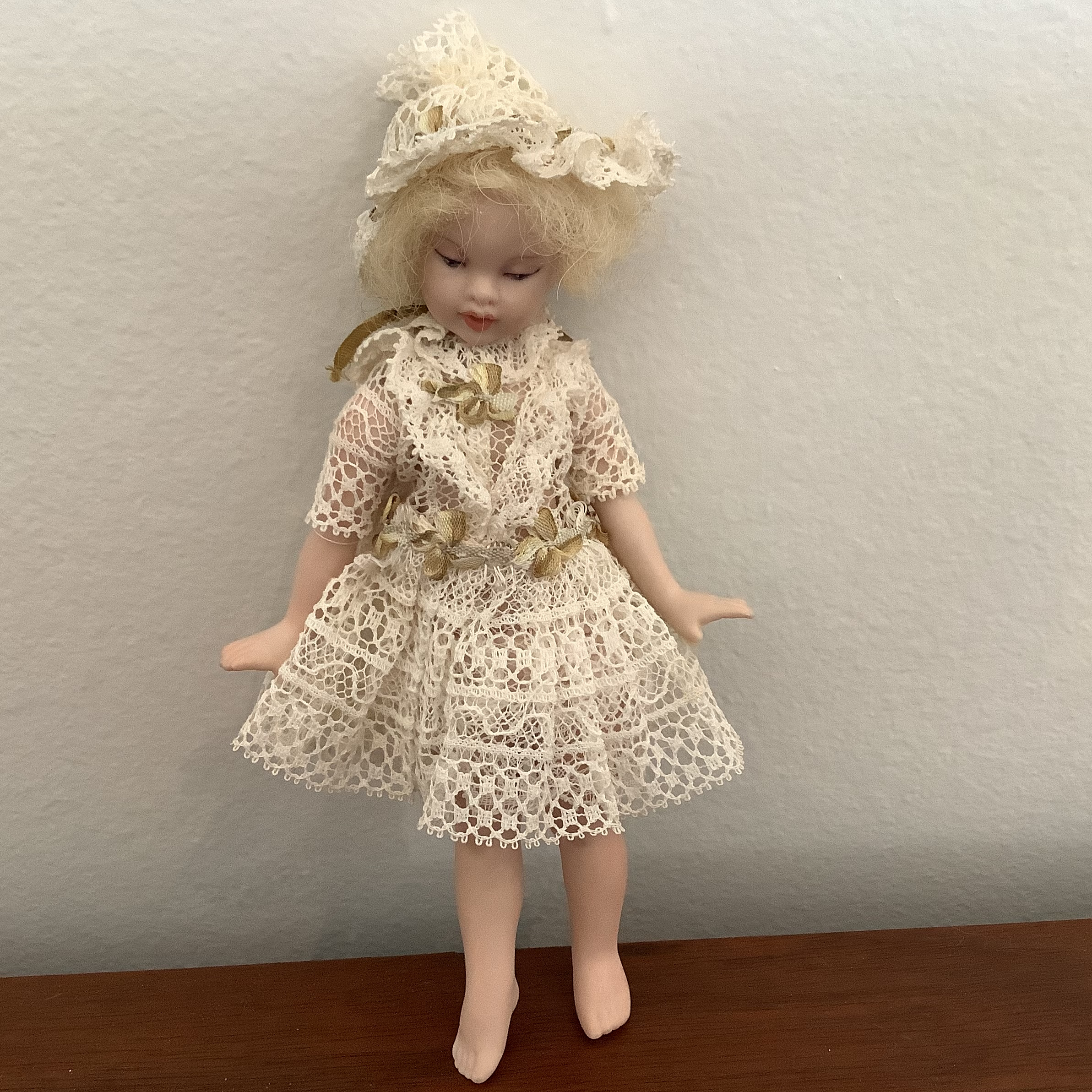 Small, blond, light-skinned doll wearing dress made entirely out of lace and matching bonnet