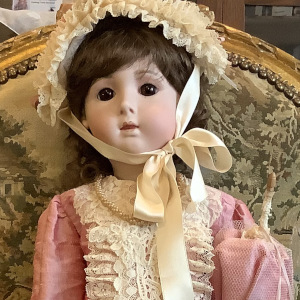 White child doll with brown curly hair in pink dress with lace trim and matching bonnet