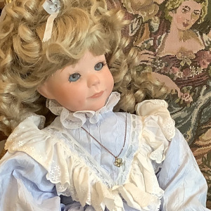 Blond white girl doll in blue dress with 80s-style white ruffle trim, hair tied back and hanging down in ringlets