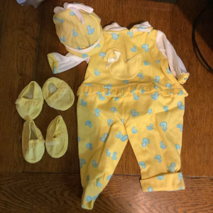 yellow romper printed with blue ducklings, with white sleeves and matching yellow duck hat and soft yellow shoes