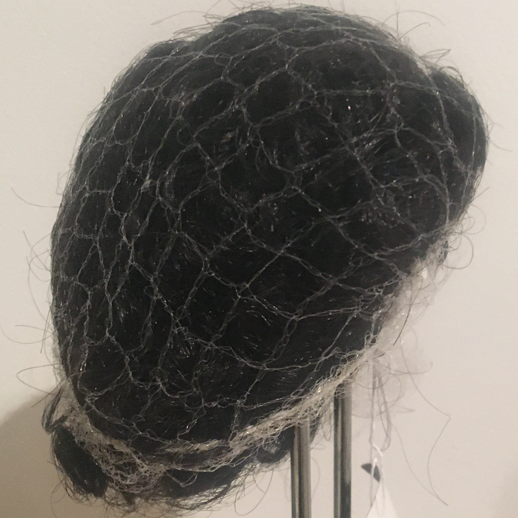 Small black wig with very tight black curls, contained in a hairnet