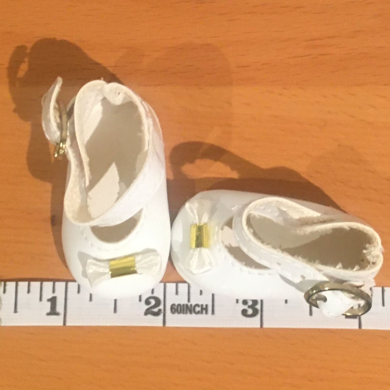 White Mary Jane shoes with gold buckles and small bows attached to the toes