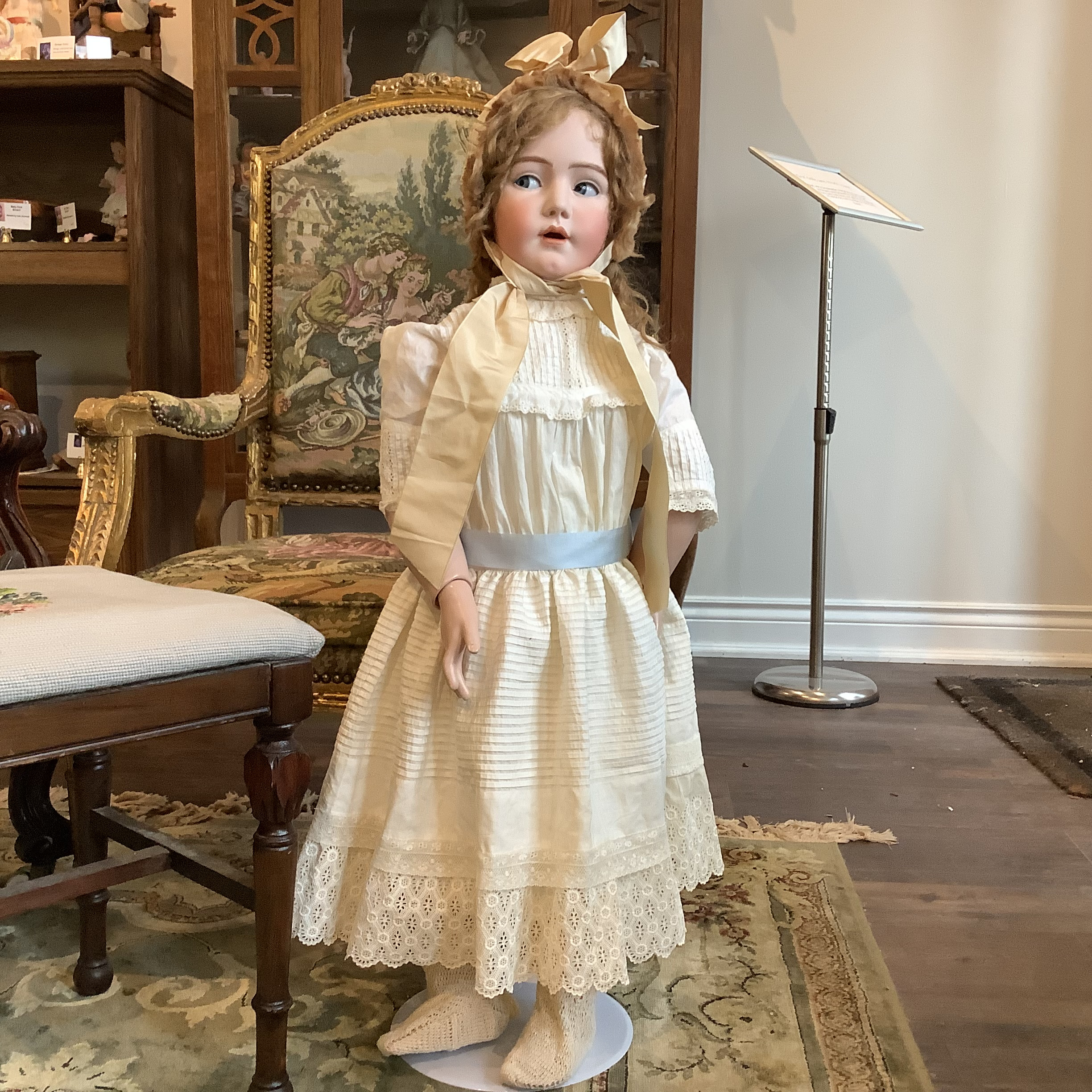 36-inch blond doll wearing a white dress with pin tucks and a beige bonnet