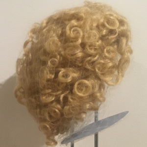 Light blond wig with allover curls, medium length, contained in a hair net