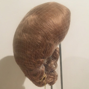 Reddish-blond or light red medium-length wig with short bangs, straight with slight wave, contained in a hair net