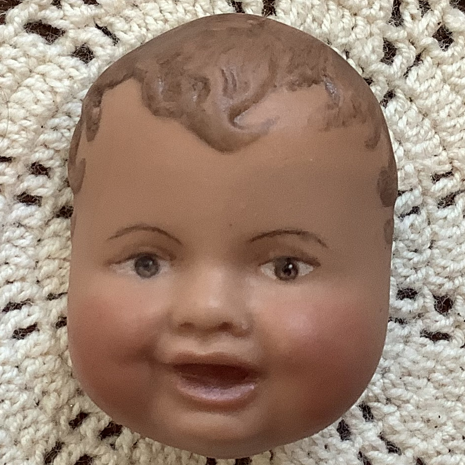 Brooch of a short-haired baby's face with dark skin and medium brown hair