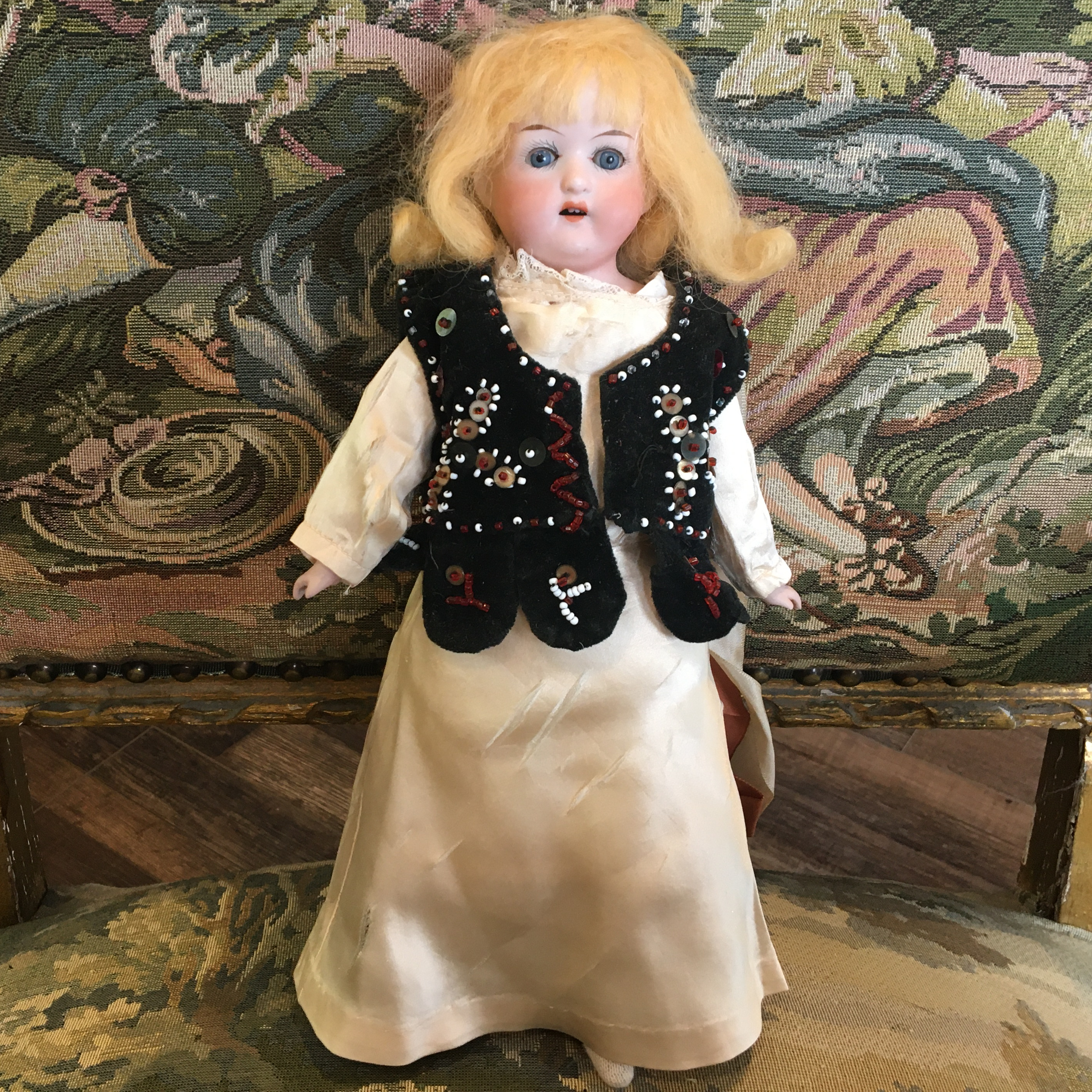 Vintage fashion doll with yellow hair and green sleep eyes wearing a yellow satin dress and a velvet dress with hand-beaded design and hanging ribbons