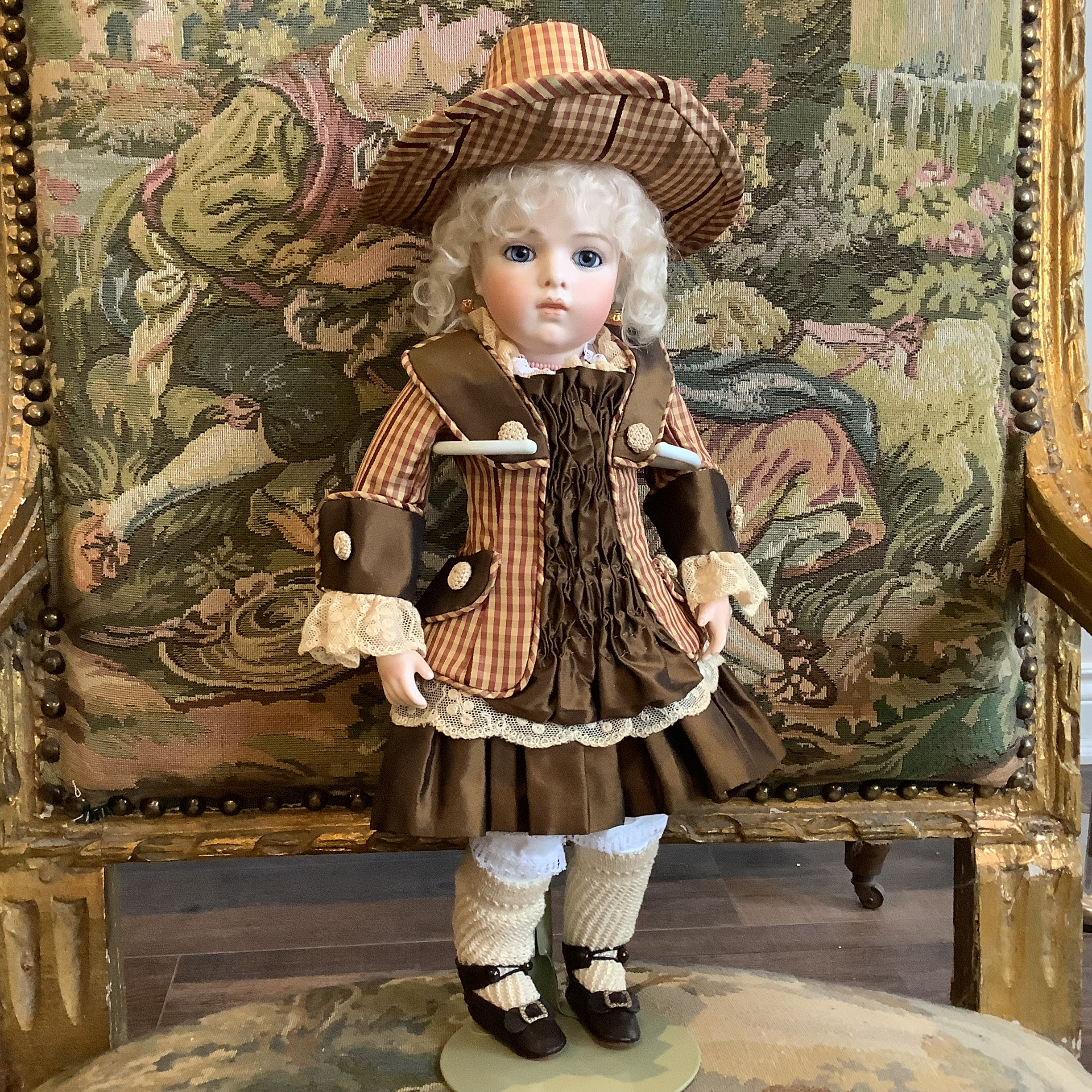 Small, white-haired doll in Tudor hat and short brown dress with lace cuffs.